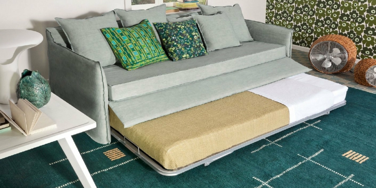 Ce salon moderne est doté d'un élégant canapé gris avec un lit gigogne, complété par des coussins verts et un tapis à motifs. Un ventilateur décoratif complète l'ambiance chic du showroom, offrant à la fois style et confort à un prix imbattable. Canape Paris by Atelier Bis