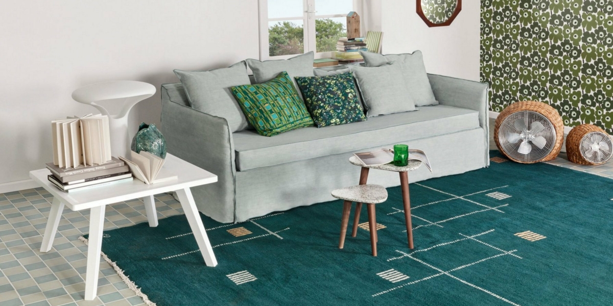 Un salon cosy avec un canapé bleu clair, des coussins à motifs, un tapis vert et des livres empilés dégage un charme parisien. Une table d'appoint blanche complète le look avec une qualité sans effort. Canape Paris by Atelier Bis