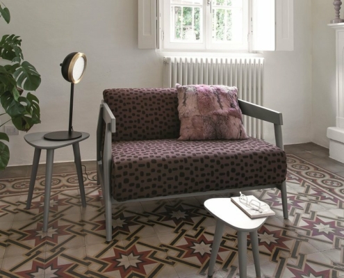 Une chambre parisienne cosy avec un canapé à motifs, des tables d'appoint, une lumière ronde et un sol en carrelage géométrique complexe. Canape Paris by Atelier Bis