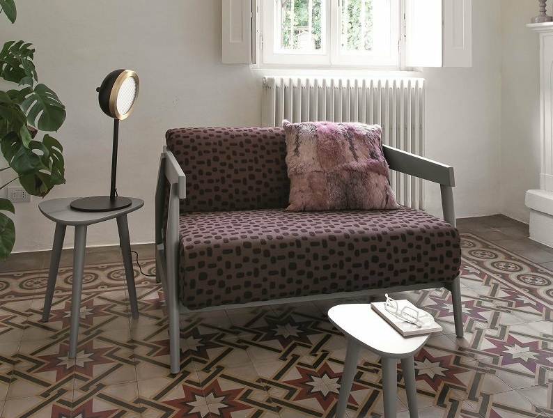 Une chambre parisienne cosy avec un canapé à motifs, des tables d'appoint, une lumière ronde et un sol en carrelage géométrique complexe. Canape Paris by Atelier Bis