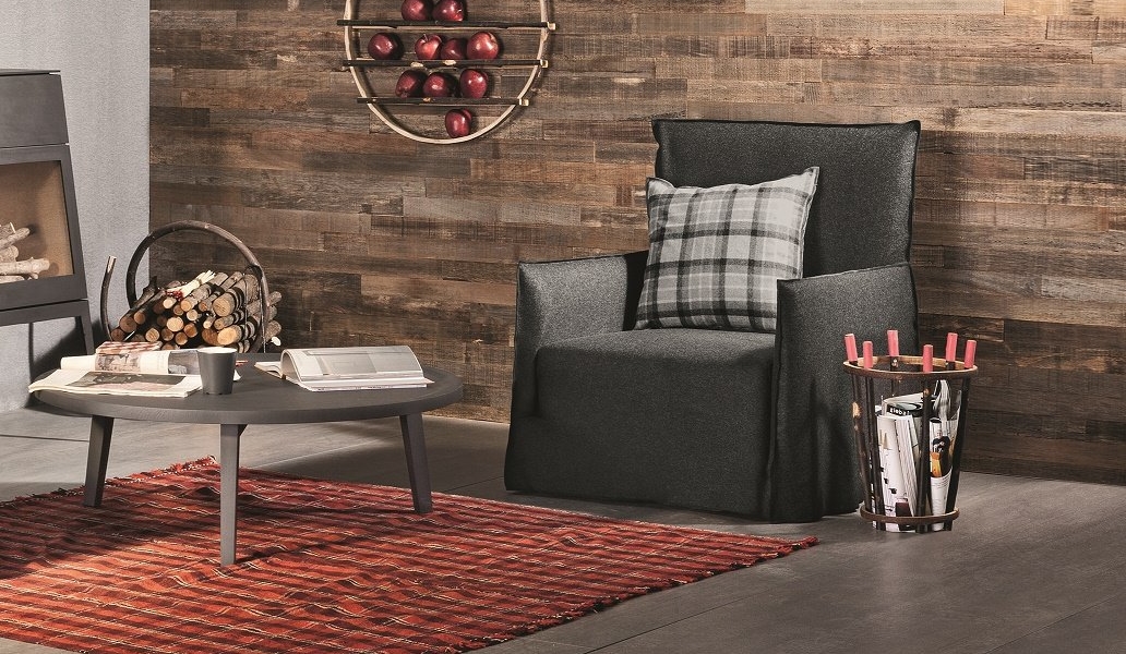 Salon parisien cosy avec fauteuil sombre, coussin à carreaux et tapis rayé. Une bibliothèque garnie de livres de qualité et de pommes rehausse le charme des boiseries, complétant l'élégant canapé. Canape Paris by Atelier Bis