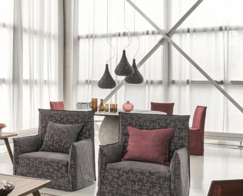 Salon moderne avec fauteuils à motifs, coussins rouges, suspensions et table avec chaises près d'une grande fenêtre, offrant une touche d'élégance parisienne. Le canapé cosy invite à la détente dans un décor chic. Canape Paris by Atelier Bis