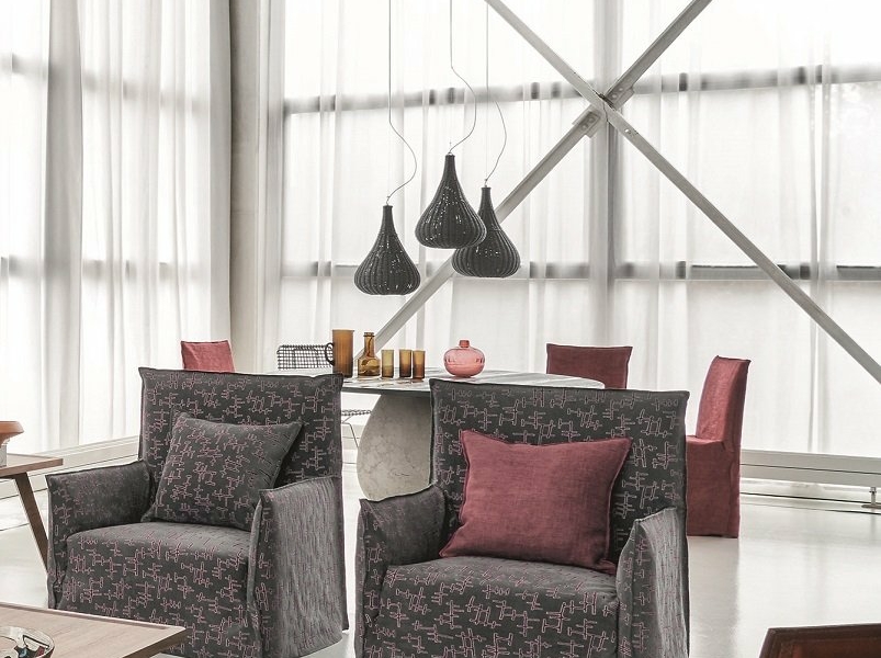 Salon moderne avec fauteuils à motifs, coussins rouges, suspensions et table avec chaises près d'une grande fenêtre, offrant une touche d'élégance parisienne. Le canapé cosy invite à la détente dans un décor chic. Canape Paris by Atelier Bis