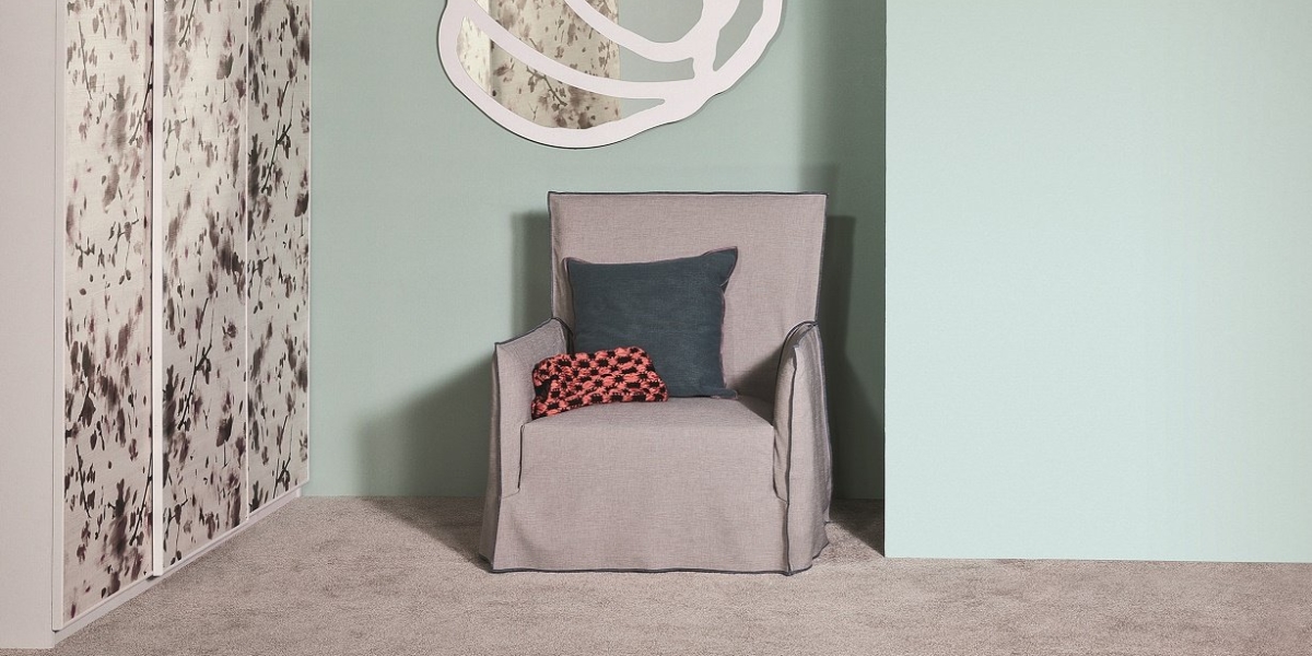 Un fauteuil gris avec un coussin bleu sarcelle et rouge se trouve dans un coin avec des murs vert clair et des œuvres d'art murales abstraites, créant une ambiance de salle d'exposition qui respire la qualité. Canape Paris by Atelier Bis