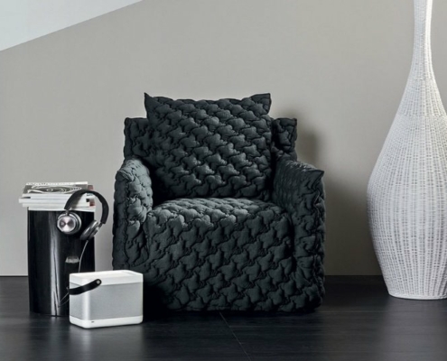 Fauteuil matelassé noir confortable dans un showroom parisien, niché à côté d'un grand vase blanc, d'une petite enceinte et d'une pile de livres avec des écouteurs. Canape Paris by Atelier Bis