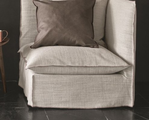 Un fauteuil beige cosy avec des coussins marron sur un sol sombre, rappelant un showroom parisien chic. Canape Paris by Atelier Bis