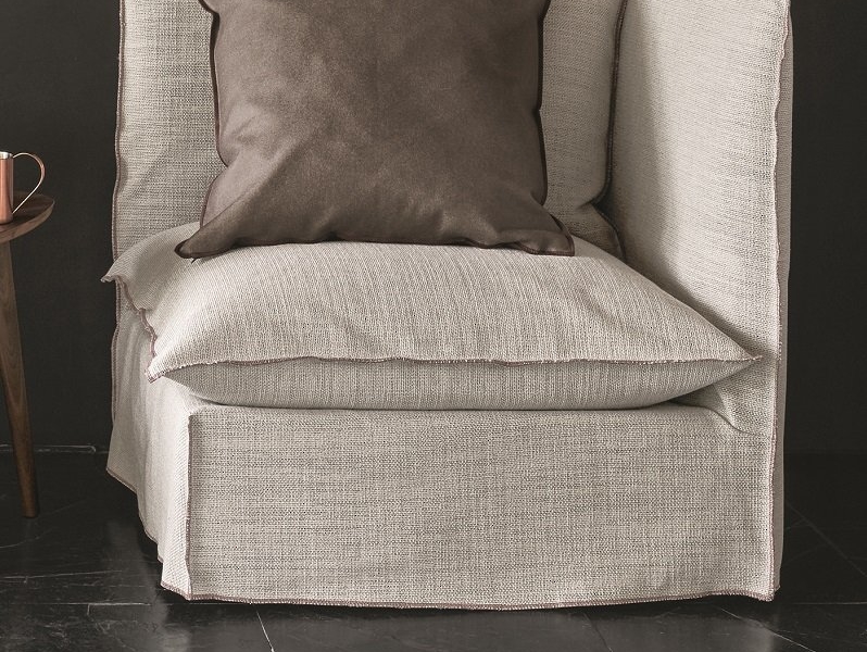 Un fauteuil beige cosy avec des coussins marron sur un sol sombre, rappelant un showroom parisien chic. Canape Paris by Atelier Bis