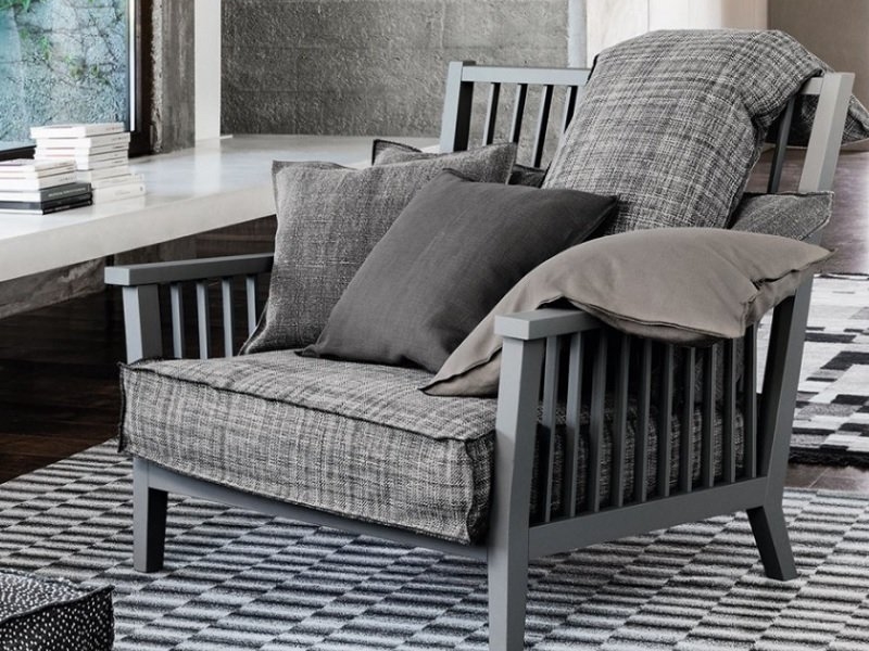 Un fauteuil gris rembourré avec des coussins à carreaux et unis repose élégamment sur un tapis à carreaux dans un salon moderne, rappelant un showroom parisien chic. Canape Paris by Atelier Bis