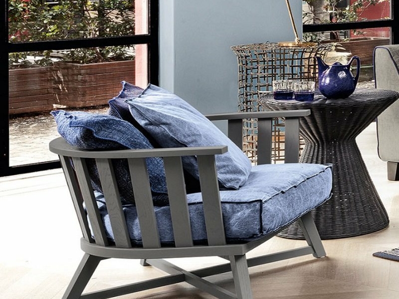 Une chaise en bois gris avec des coussins bleus trône à côté d'une petite table ronde avec une théière, installée à l'intérieur près d'une grande fenêtre. Cette configuration élégante respire le charme parisien, offrant un rapport qualité-prix et style inégalé. Canape Paris by Atelier Bis
