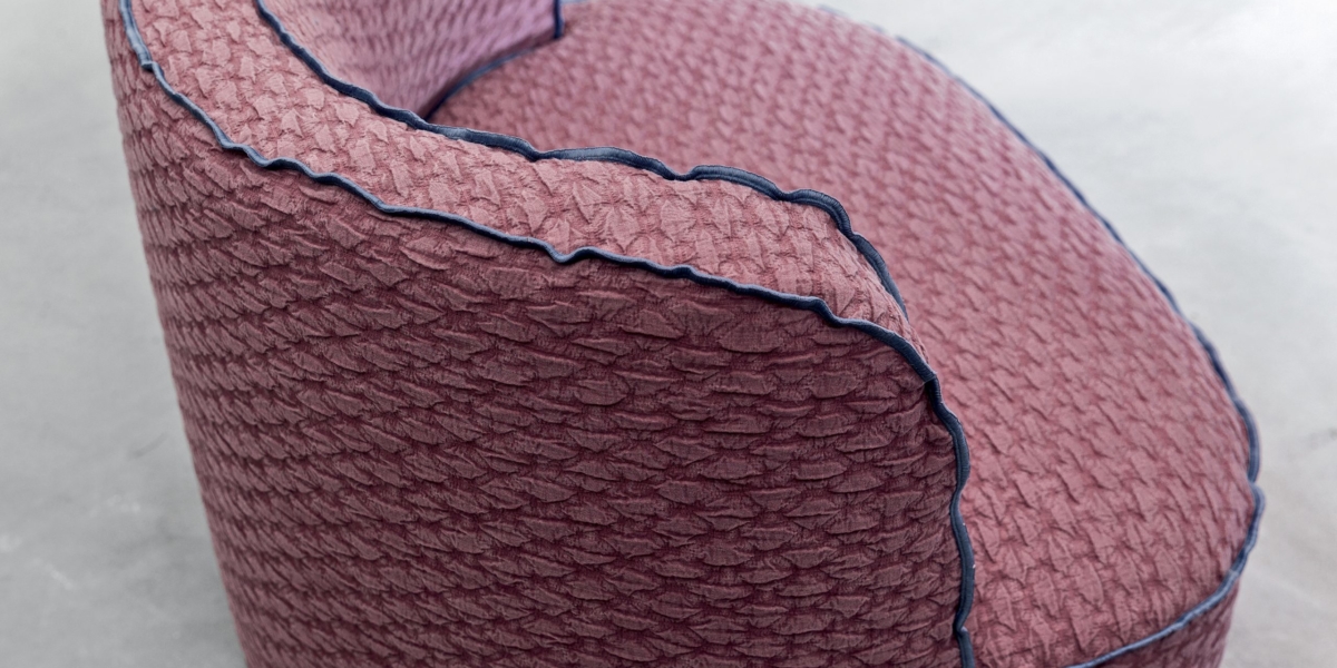 Chaise rembourrée texturée rose avec passepoil bleu sur fond gris clair, mettant en valeur l'élégance de qualité showroom. Canape Paris by Atelier Bis