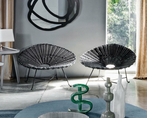 Salle d'exposition moderne comprenant deux chaises tissées noires, un canapé confortable, des œuvres d'art murales abstraites et des objets décoratifs sur une table ronde. Canape Paris by Atelier Bis