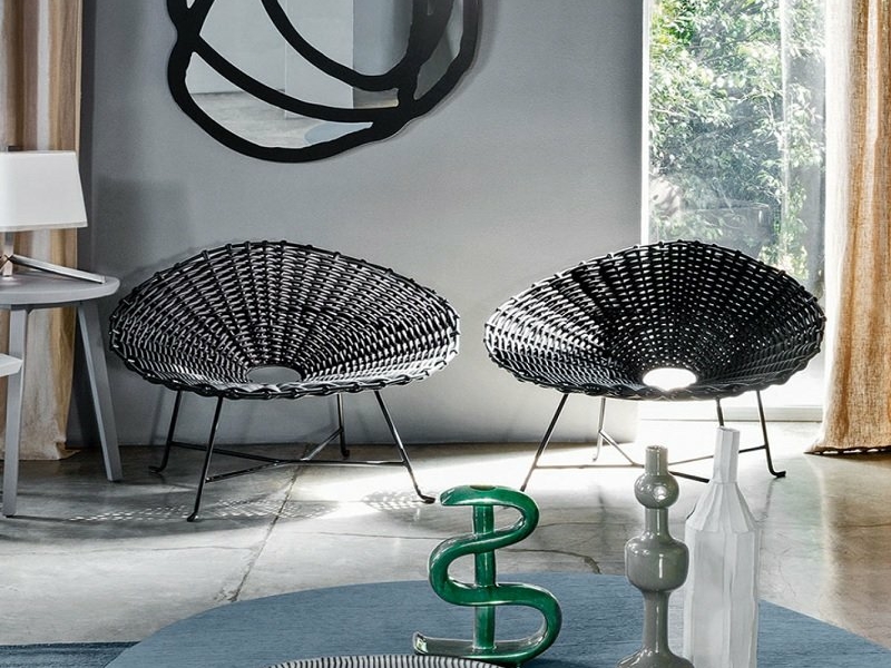 Salle d'exposition moderne comprenant deux chaises tissées noires, un canapé confortable, des œuvres d'art murales abstraites et des objets décoratifs sur une table ronde. Canape Paris by Atelier Bis