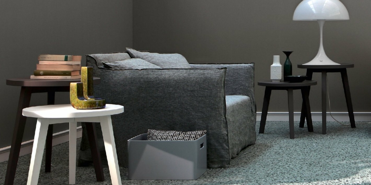 Salon moderne avec un fauteuil gris, des tables d'appoint, des livres, une lampe et des objets de décoration sur un tapis bleu texturé, le tout reflétant la qualité et l'ambiance chic que l'on attend d'un cadre parisien. Canape Paris by Atelier Bis