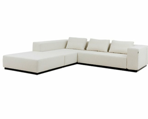 Un canapé sectionnel chic en forme de L blanc avec coussins se dresse élégamment sur un fond blanc immaculé, rappelant l'esthétique raffinée d'un showroom parisien. Canape Paris by Atelier Bis