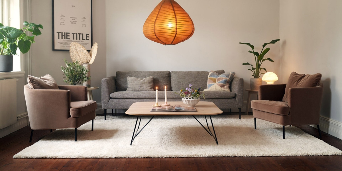 Salon cosy avec un canapé gris, des fauteuils marron, une table en bois et une grande suspension sur un tapis blanc, respirant la qualité parisienne. Canape Paris by Atelier Bis