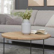 Canapé gris avec coussins, table basse ronde en bois avec vase et livre, art abstrait et table d'appoint dans un salon. Canape Paris by Atelier Bis