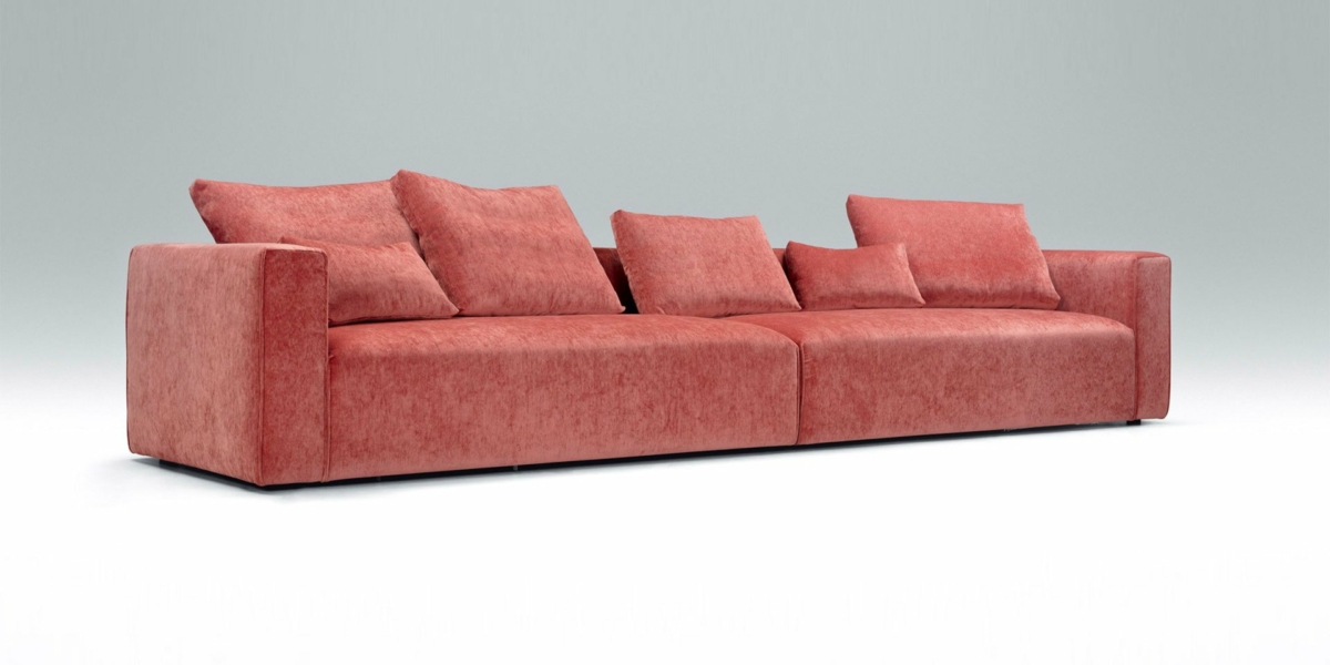 Un canapé en velours rouge avec plusieurs coussins assortis se dresse élégamment sur un fond gris clair uni, comme s'il était présenté dans un showroom parisien chic. Canape Paris by Atelier Bis