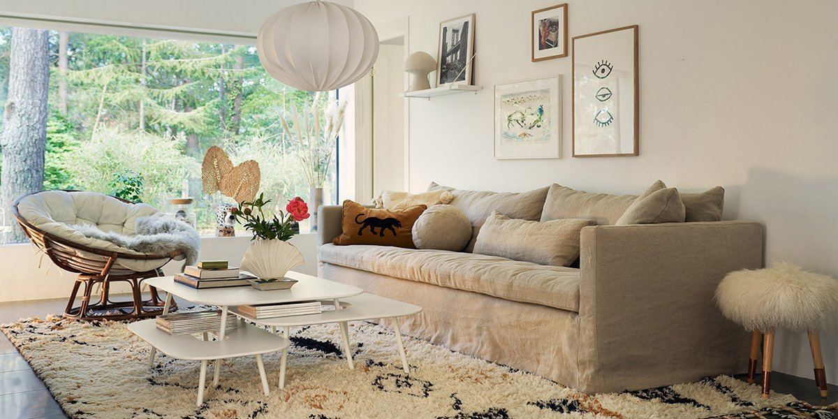 Salon confortable avec canapé beige, fauteuil rond et tables basses blanches. Profitez de la vue sur la nature de qualité showroom à travers la grande fenêtre. Canape Paris by Atelier Bis