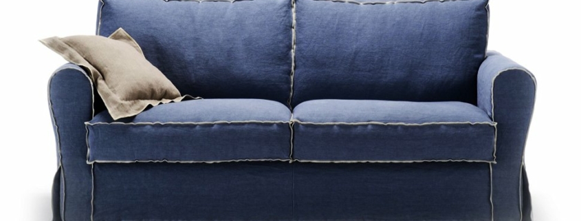 Un canapé deux places bleu avec un passepoil beige exquis et un coussin beige moelleux sur le côté gauche, incarnant l'élégance intemporelle et la qualité que l'on peut s'attendre à trouver dans un appartement parisien chic. Canape Paris by Atelier Bis