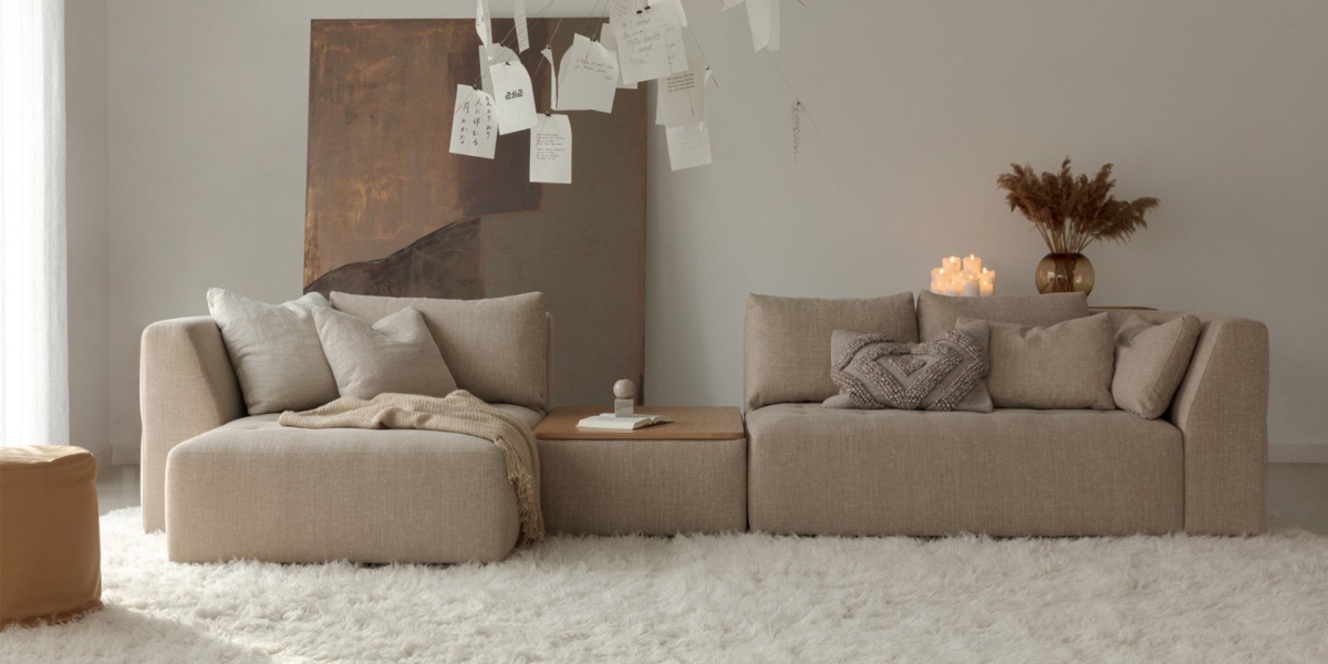 Salon minimaliste avec canapés beiges et canapé, complété par un tapis moelleux et un éclairage chaleureux. Un tableau et des papiers suspendus ajoutent de la qualité à la décoration, rappelant un showroom chic. Canape Paris by Atelier Bis