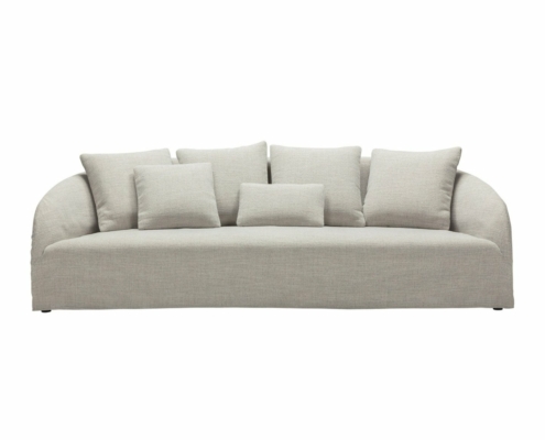 Un canapé rembourré gris clair avec cinq coussins assortis, doté d'un dossier incurvé et d'un design minimaliste, reflétant l'élégance d'un showroom parisien. Canape Paris by Atelier Bis