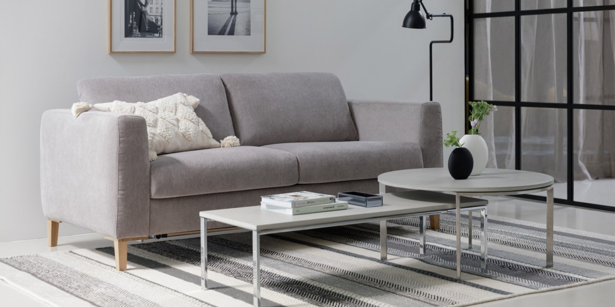 Salon moderne avec un canapé gris, des coussins décoratifs, deux tables basses rondes et des œuvres d'art encadrées au mur, décoré comme une salle d'exposition parisienne. Canape Paris by Atelier Bis