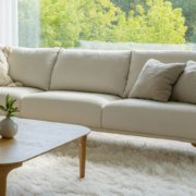 Salon moderne avec un canapé blanc, une table basse en bois et un tapis moelleux, rappelant un showroom parisien, donnant sur une vue extérieure verte et vibrante. Canape Paris by Atelier Bis