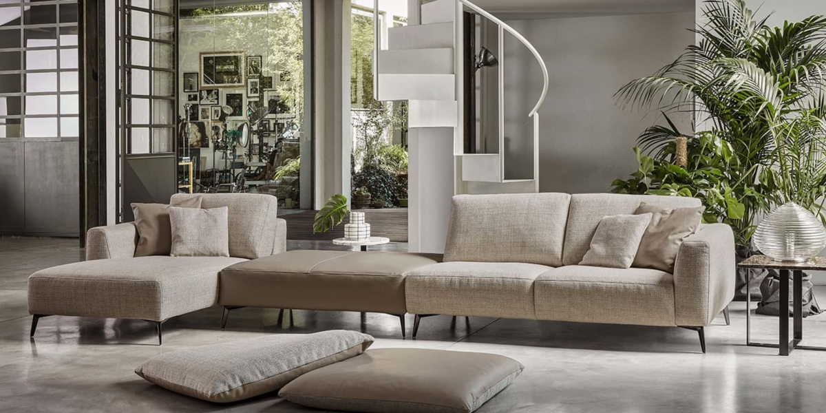 Un salon chic et moderne à Paris comprend un canapé sectionnel beige, des coussins douillets, un escalier en colimaçon saisissant et une abondance de grandes plantes pour une touche de nature. Canape Paris by Atelier Bis