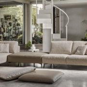 Un salon chic et moderne à Paris comprend un canapé sectionnel beige, des coussins douillets, un escalier en colimaçon saisissant et une abondance de grandes plantes pour une touche de nature. Canape Paris by Atelier Bis