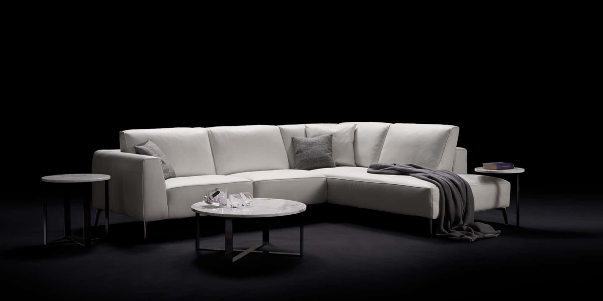 Canapé sectionnel blanc avec coussins et jeté gris, flanqué de tables rondes sur fond noir, reflétant l'élégance chic du décor parisien, où la qualité rencontre le style sans effort. Canape Paris by Atelier Bis