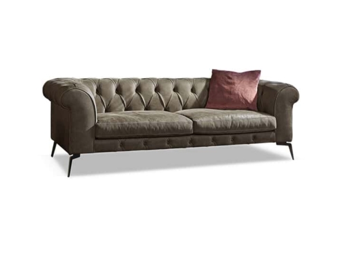 Ce canapé capitonné vert élégant, avec ses accoudoirs roulés et ses pieds élancés, respire le charme parisien. Un coussin marron unique ajoute une touche de sophistication sur le côté droit, mettant en valeur sa qualité exceptionnelle. Canape Paris by Atelier Bis