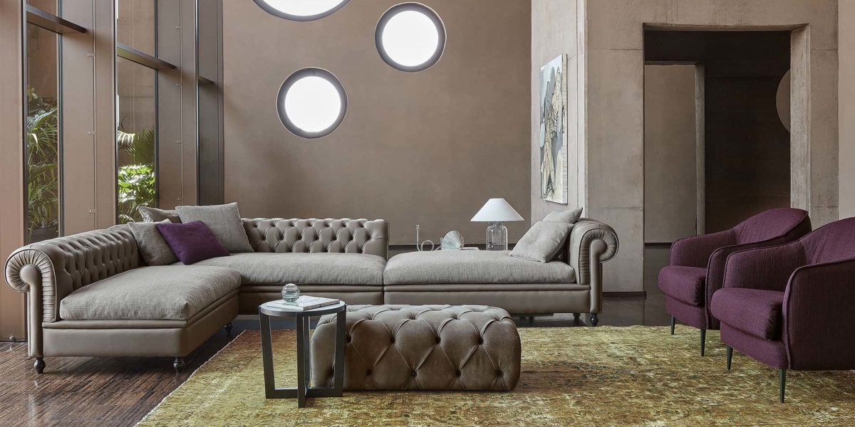 Salon sophistiqué avec un canapé sectionnel taupe, des chaises violettes, des fenêtres rondes et un tapis texturé qui respire la qualité. Canape Paris by Atelier Bis