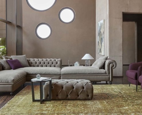 Salon sophistiqué avec un canapé sectionnel taupe, des chaises violettes, des fenêtres rondes et un tapis texturé qui respire la qualité. Canape Paris by Atelier Bis