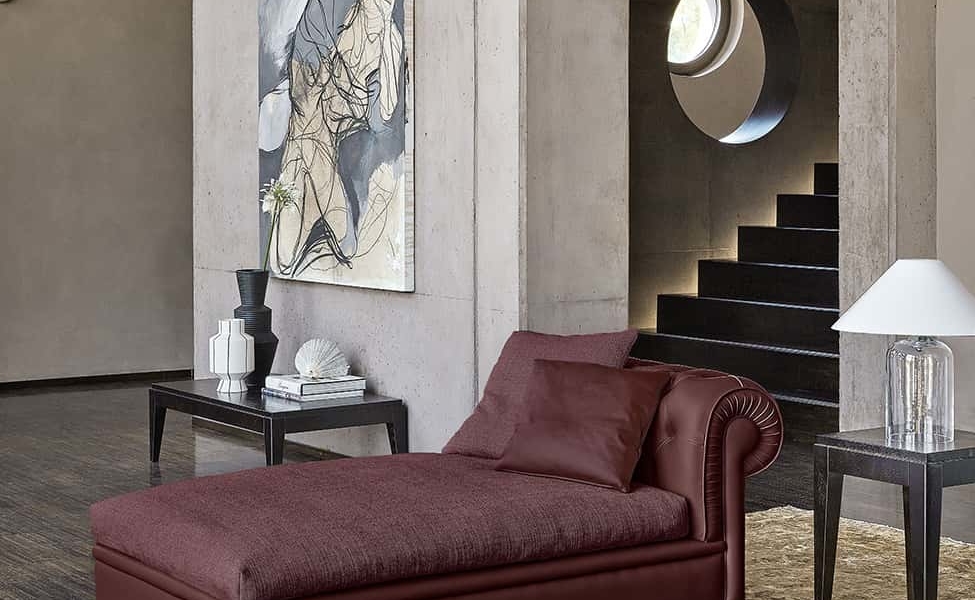 Showroom moderne avec chaise longue marron, œuvres d'art abstraites et vitrine circulaire. Découvrez un décor minimaliste avec des murs en béton gris qui respirent la qualité et le style. Canape Paris by Atelier Bis