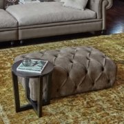 Luxueux salon parisien avec un pouf capitonné, une table d'appoint ronde avec un magazine de qualité, un cendrier en verre et un canapé moelleux. Canape Paris by Atelier Bis