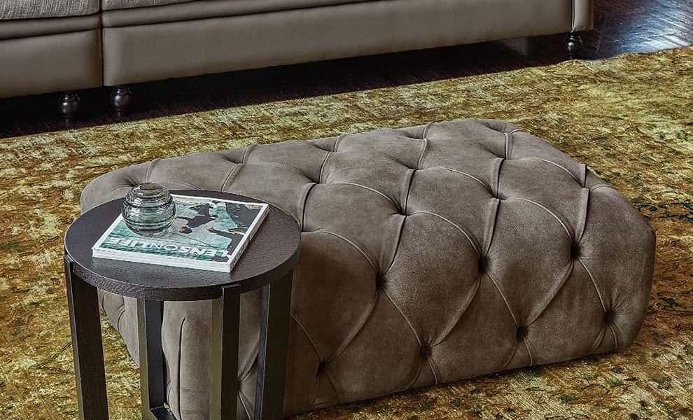 Luxueux salon parisien avec un pouf capitonné, une table d'appoint ronde avec un magazine de qualité, un cendrier en verre et un canapé moelleux. Canape Paris by Atelier Bis