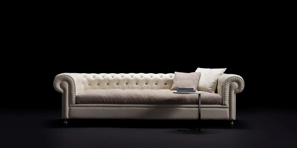 Élégant canapé capitonné de couleur crème avec des coussins beiges et une petite table contenant des livres, présenté dans notre salle d'exposition sur un fond noir, offrant une qualité inégalée à un prix imbattable. Canape Paris by Atelier Bis