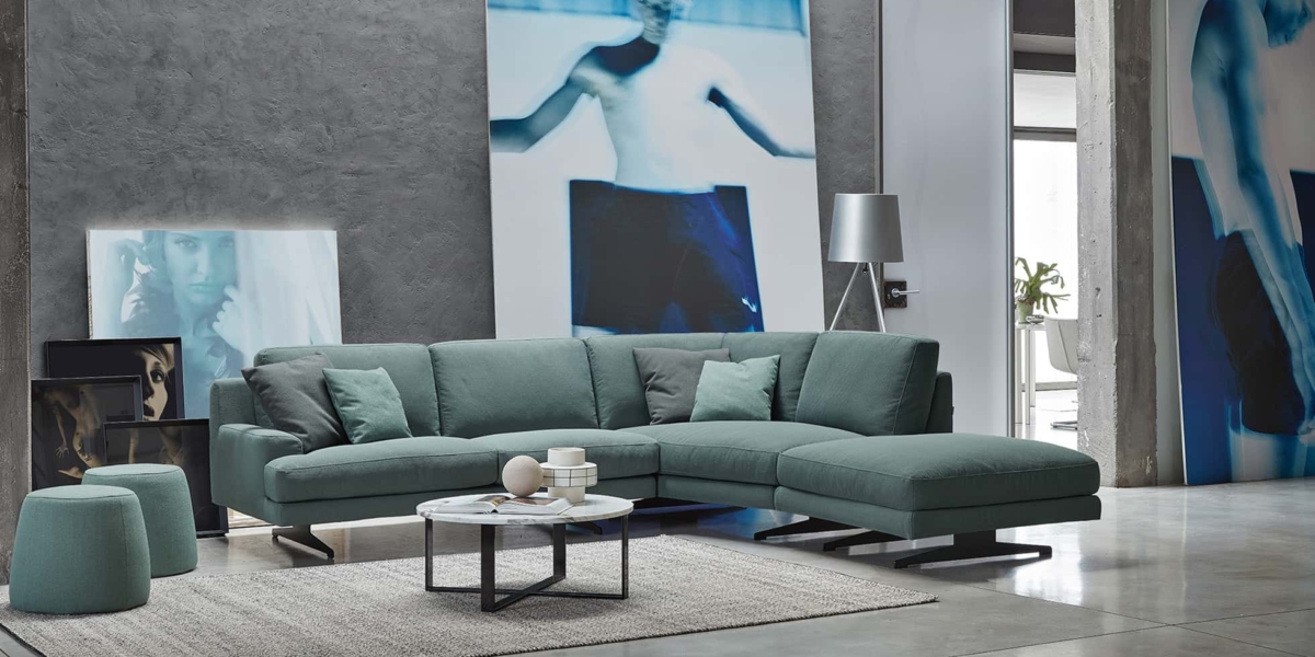 Salon moderne avec un canapé sectionnel bleu sarcelle, une table basse ronde et de grandes œuvres d'art abstraites sur des murs en béton, offrant un mélange parfait de style et de qualité qui semble tout droit sorti d'un appartement parisien chic. Canape Paris by Atelier Bis