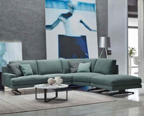 Salon moderne avec un canapé sectionnel bleu sarcelle, une table basse ronde et de grandes œuvres d'art abstraites sur des murs en béton, offrant un mélange parfait de style et de qualité qui semble tout droit sorti d'un appartement parisien chic. Canape Paris by Atelier Bis