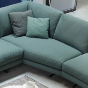 Un canapé sectionnel vert avec deux coussins orne un salon parisien moderne, flanqué d'une table basse ronde ornée d'objets de décoration, dégageant un air de qualité. Canape Paris by Atelier Bis