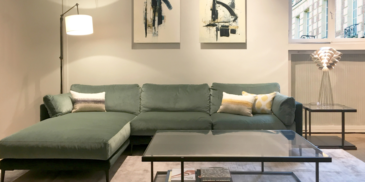 Un salon moderne et sophistiqué à Paris, doté d'un luxueux canapé vert, de peintures abstraites, d'une élégante table basse en verre et d'un élégant lampadaire. Canape Paris by Atelier Bis