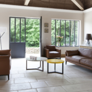 Salon moderne avec canapés en cuir, tables rondes, grandes fenêtres et vue sur la verdure extérieure, présentant un design de qualité showroom à un prix imbattable. Canape Paris by Atelier Bis