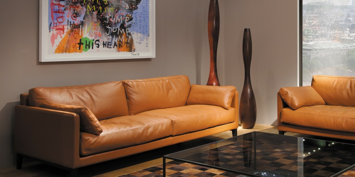 Salon moderne doté d'un canapé en cuir beige de haute qualité, accentué par de hautes sculptures en bois et un tableau coloré au-dessus de l'élégante table basse en verre, apportant une touche d'élégance parisienne. Canape Paris by Atelier Bis