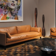 Salon moderne doté d'un canapé en cuir beige de haute qualité, accentué par de hautes sculptures en bois et un tableau coloré au-dessus de l'élégante table basse en verre, apportant une touche d'élégance parisienne. Canape Paris by Atelier Bis