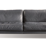 Un canapé chic et moderne en cuir gris foncé, agrémenté de deux coussins moelleux, sur fond blanc immaculé rappelant l'élégance parisienne. Canape Paris by Atelier Bis