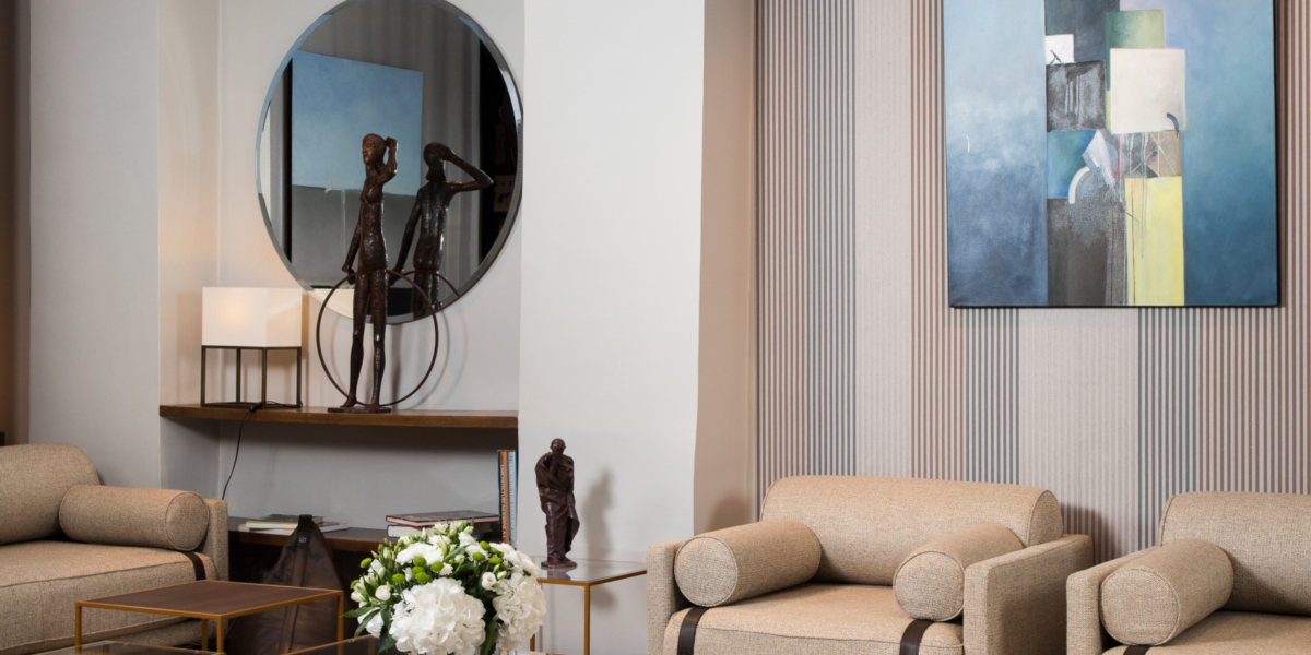 Salon moderne avec canapés beiges, table basse ronde, tableaux abstraits et suspensions. Le tapis beige contraste élégamment avec le sol foncé, apportant une touche de qualité parisienne. Canape Paris by Atelier Bis
