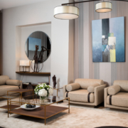 Salon moderne avec canapés beiges, table basse ronde, tableaux abstraits et suspensions. Le tapis beige contraste élégamment avec le sol foncé, apportant une touche de qualité parisienne. Canape Paris by Atelier Bis