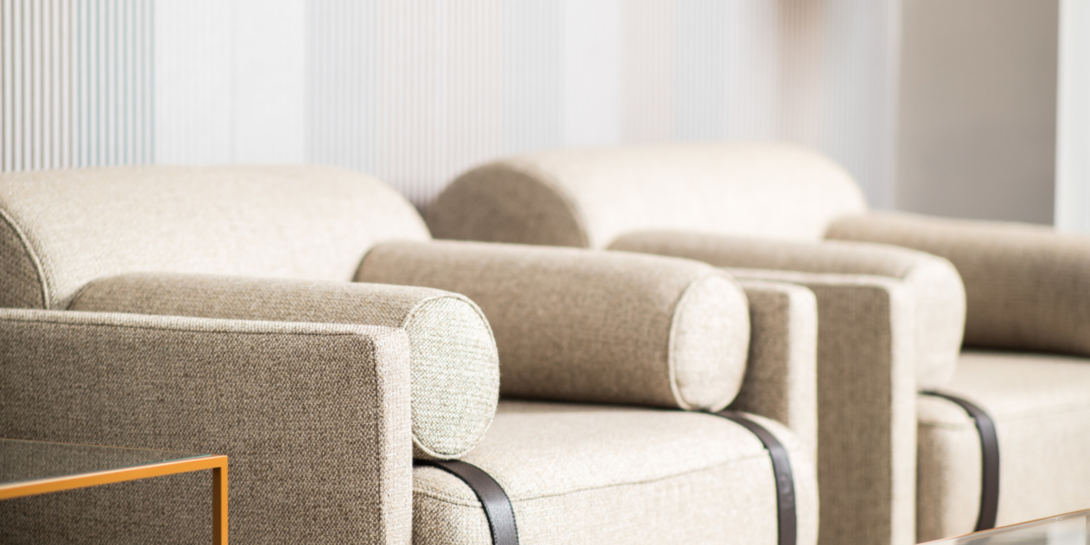 Salon moderne avec une touche d'esprit parisien, avec des fauteuils beiges, une table basse en verre épurée et un tableau abstrait sur un mur rayé. La pièce maîtresse est un canapé moelleux qui complète l'atmosphère sophistiquée qui s'apparente à un élégant showroom. Canape Paris by Atelier Bis