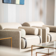 Salon moderne avec une touche d'esprit parisien, avec des fauteuils beiges, une table basse en verre épurée et un tableau abstrait sur un mur rayé. La pièce maîtresse est un canapé moelleux qui complète l'atmosphère sophistiquée qui s'apparente à un élégant showroom. Canape Paris by Atelier Bis