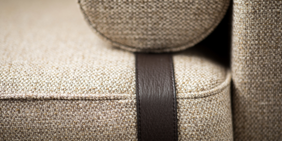 Gros plan d'un canapé texturé beige avec un détail de sangle en cuir foncé, présentant une qualité exceptionnelle qui en fait une pièce remarquable dans n'importe quelle salle d'exposition. Canape Paris by Atelier Bis